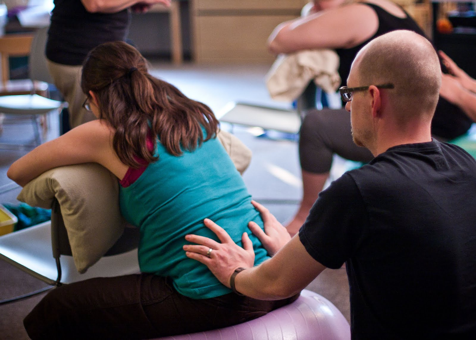 Husband rubbing back of pregnant wife sitting on an exercise ball in The Bradley Method class.